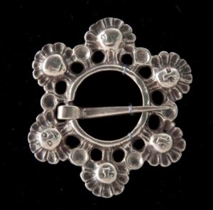 Brooch with a circle of masques surrounding a ring with a loose pin - Norwegian Metalworking