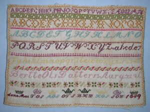 alphabet sampler done on a natural colored canvas-backing in cross-stitch using two strands of wool yarn - Textiles