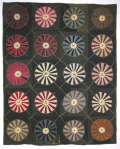 This pieced quilt was made predominantly from wool fabrics in a pattern known as Wagon Wheel or Wheel of Chance - Textiles