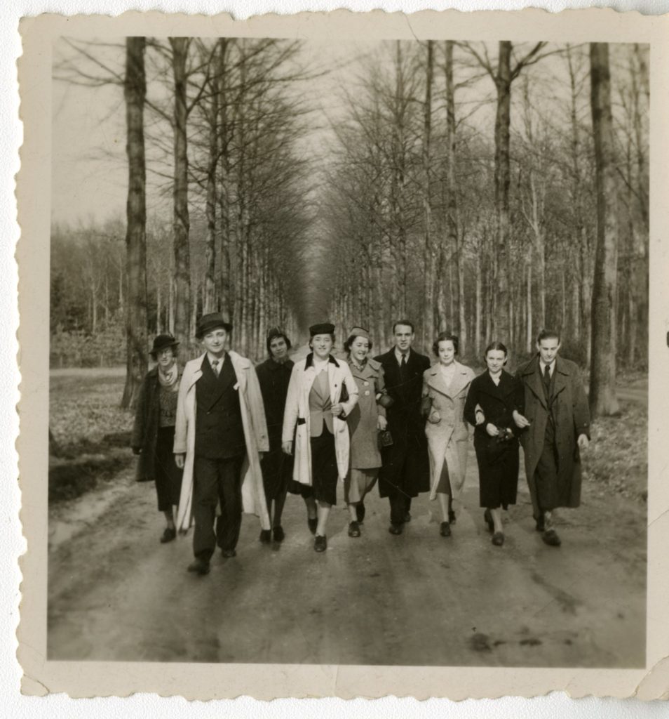 Group of men and women walking down a tree-lined road.