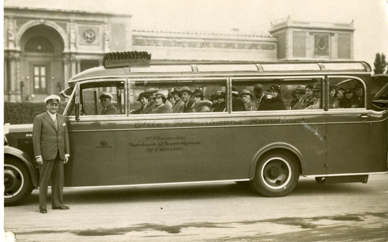A man poses outside of a long bus with many people inside.
