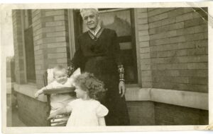 Grandma Johnson poses with two children. One in highchair and one standing in front.