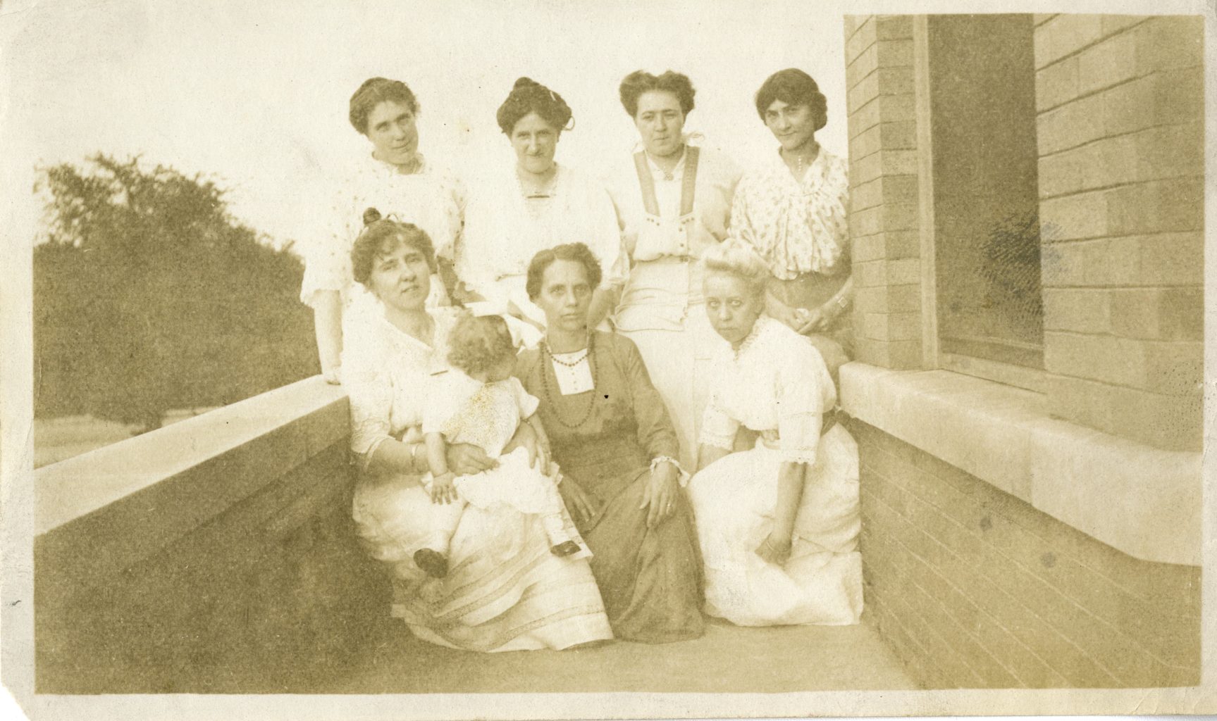 Seven women and young girl pose for photograph outside of building.