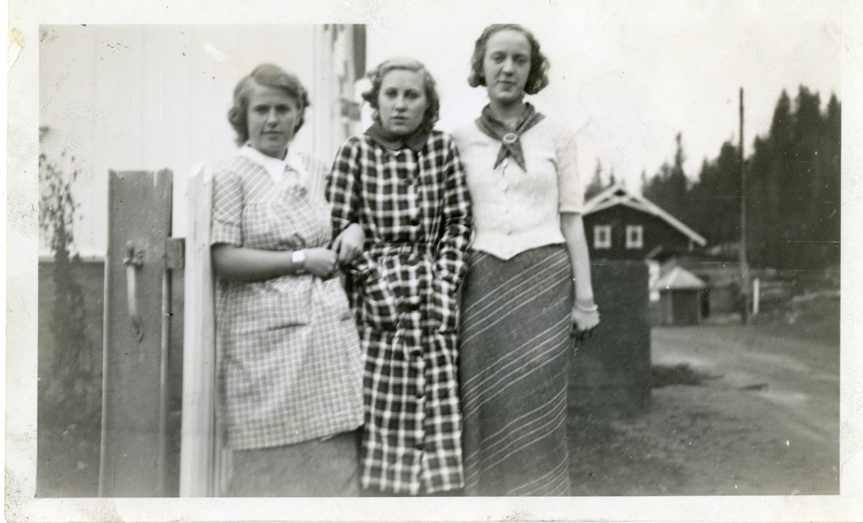 Three unidentified women stand along a fence. Norway