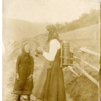 Woman and child stand on road, woman knitting, child smiling.