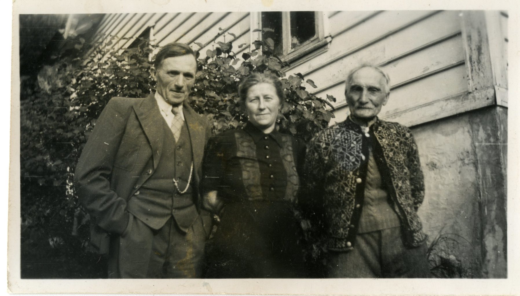 Three individuals posing for a photo outside of a house.