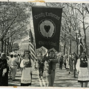 Trinity Lutheran Church School parade down street. Women in folk dresses, Norwegian and American flags flying.