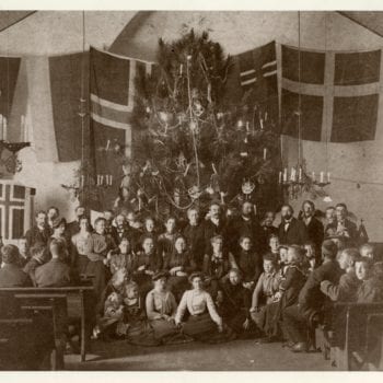 Large group photo of members of the church. Christmas tree decorated and Norwegian flag behind.