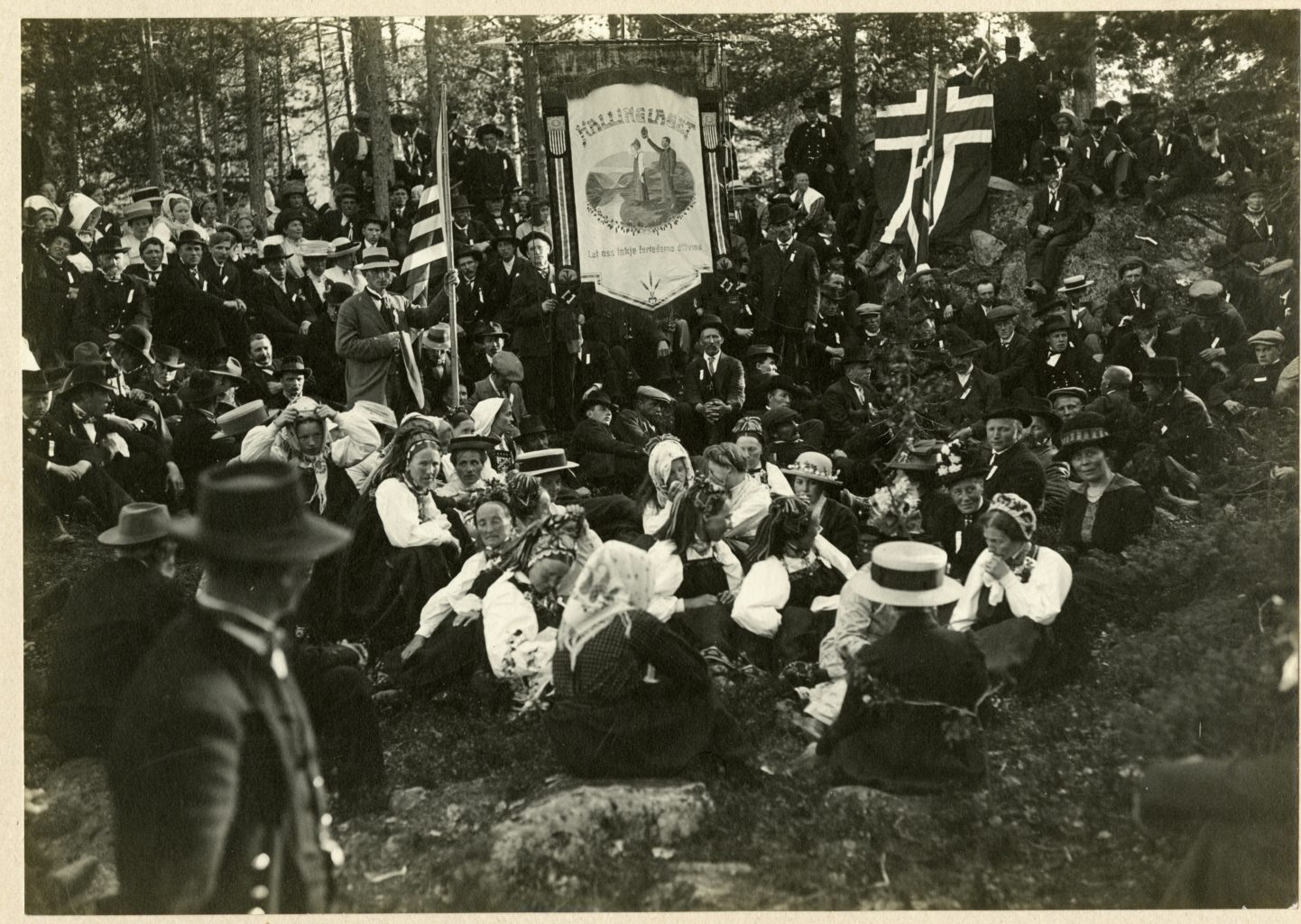 Large group outside in national dress with Norwegian and American flags flying.