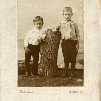 Two boys pose next to a tree stump in a studio.