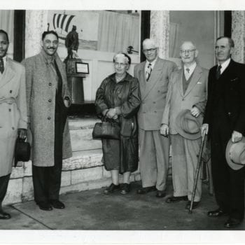 Group of five men and woman posing for a photo outside of a building.