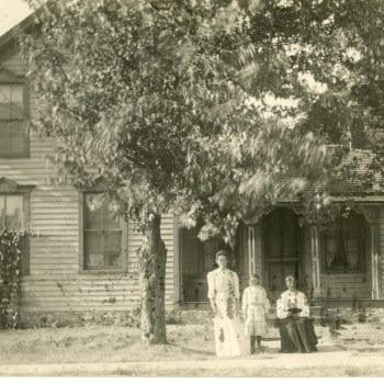 Three women pose for a photograph outside a house.