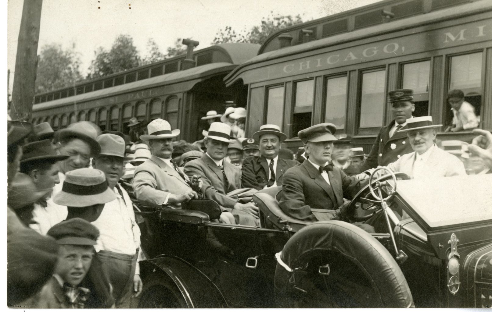 Large group of men, some in car, outside of train.