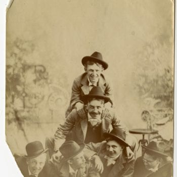 Six men lay on top of each other for photo in studio.