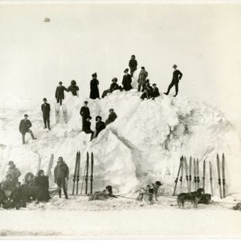 Group with sled dogs pose on snow pile.