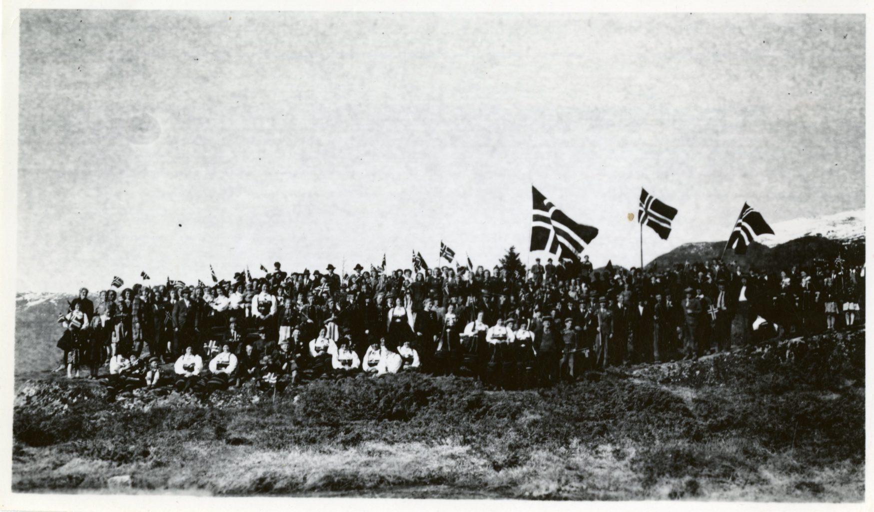 A large crowd of Norwegians in national dress with Norwegian flags flying.