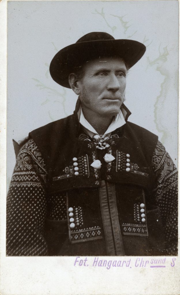 Man poses in studio in national dress and hat.