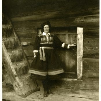 Woman in national dress poses for photo by building.