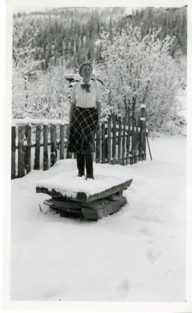 A woman standing on a wood pile in winter.