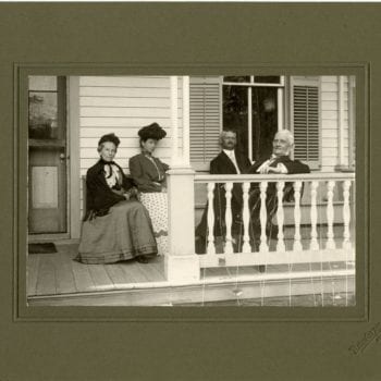 Four people sit together on the porch at the Koren Parsonage