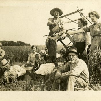 Group of men, women, and children sit in a field, rest from work.