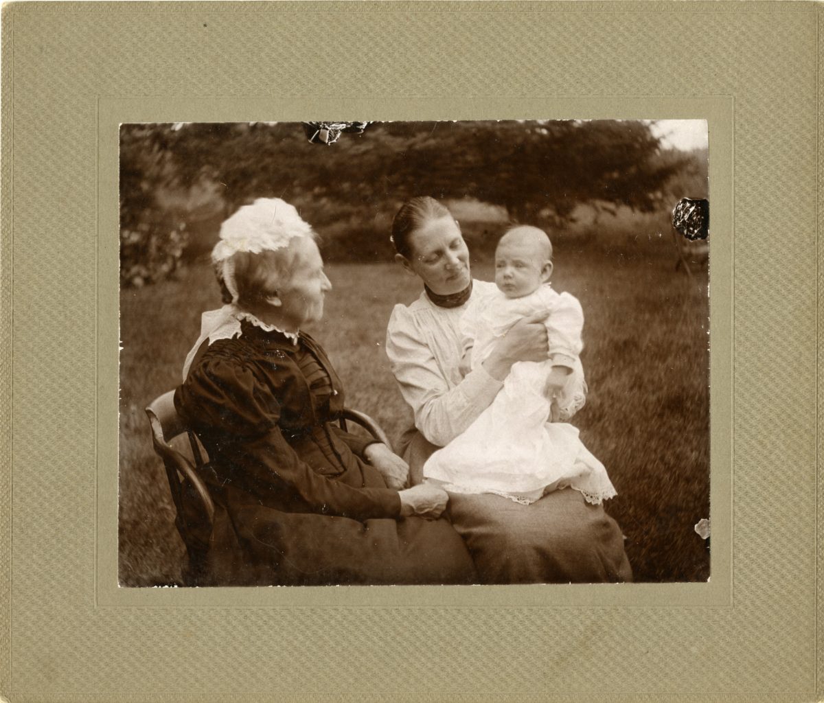 Elderly woman, young woman, and baby sit together outside.
