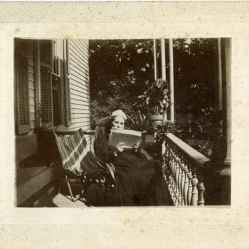 Woman sits on porch reading.