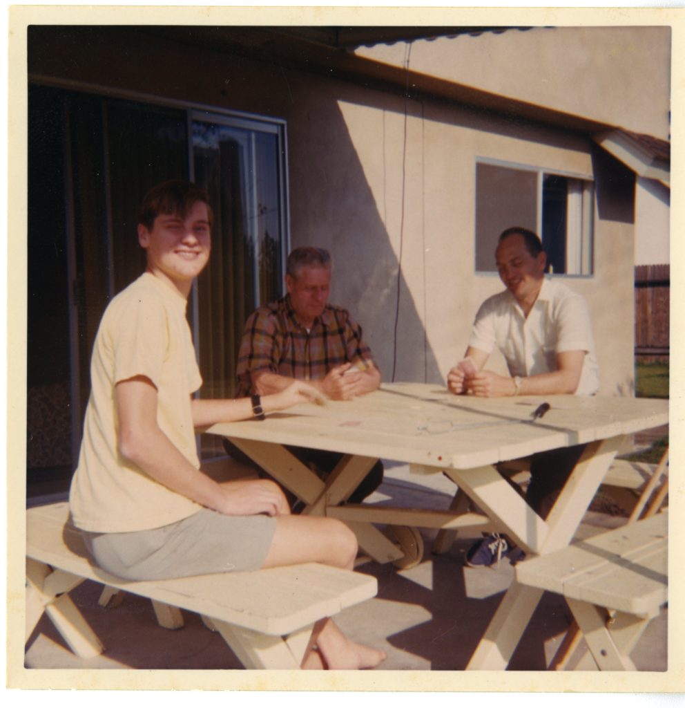 Three men sit around a picnic table.