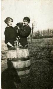 Two girls holding one dog and the other dog in a wheel barrel.