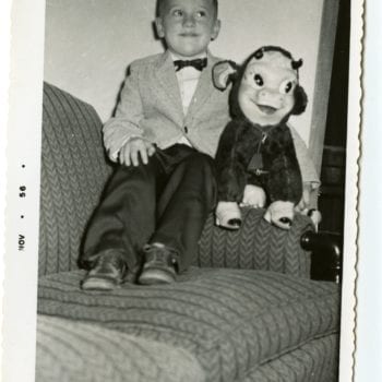 A boy sits on a couch with stuffed animal.