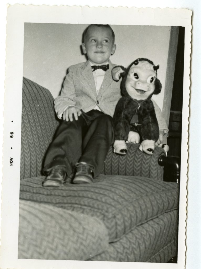A boy sits on a couch with stuffed animal.